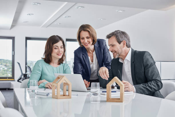 Trois personnes qui discutent autour d'un bureau, avec des maquettes de maisons en bois