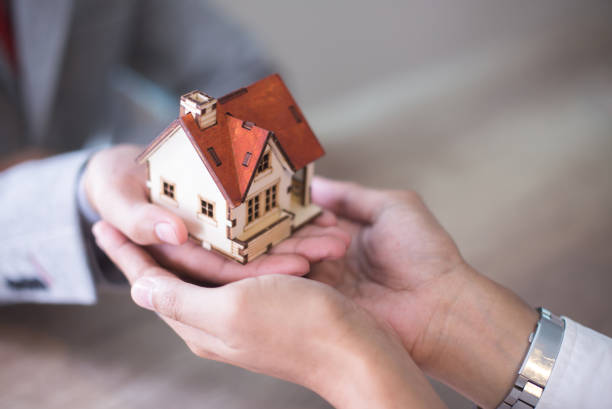 Mains d'une personne qui confie une petite maison en bois à une autre