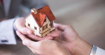 Mains d'une personne qui confie une petite maison en bois à une autre